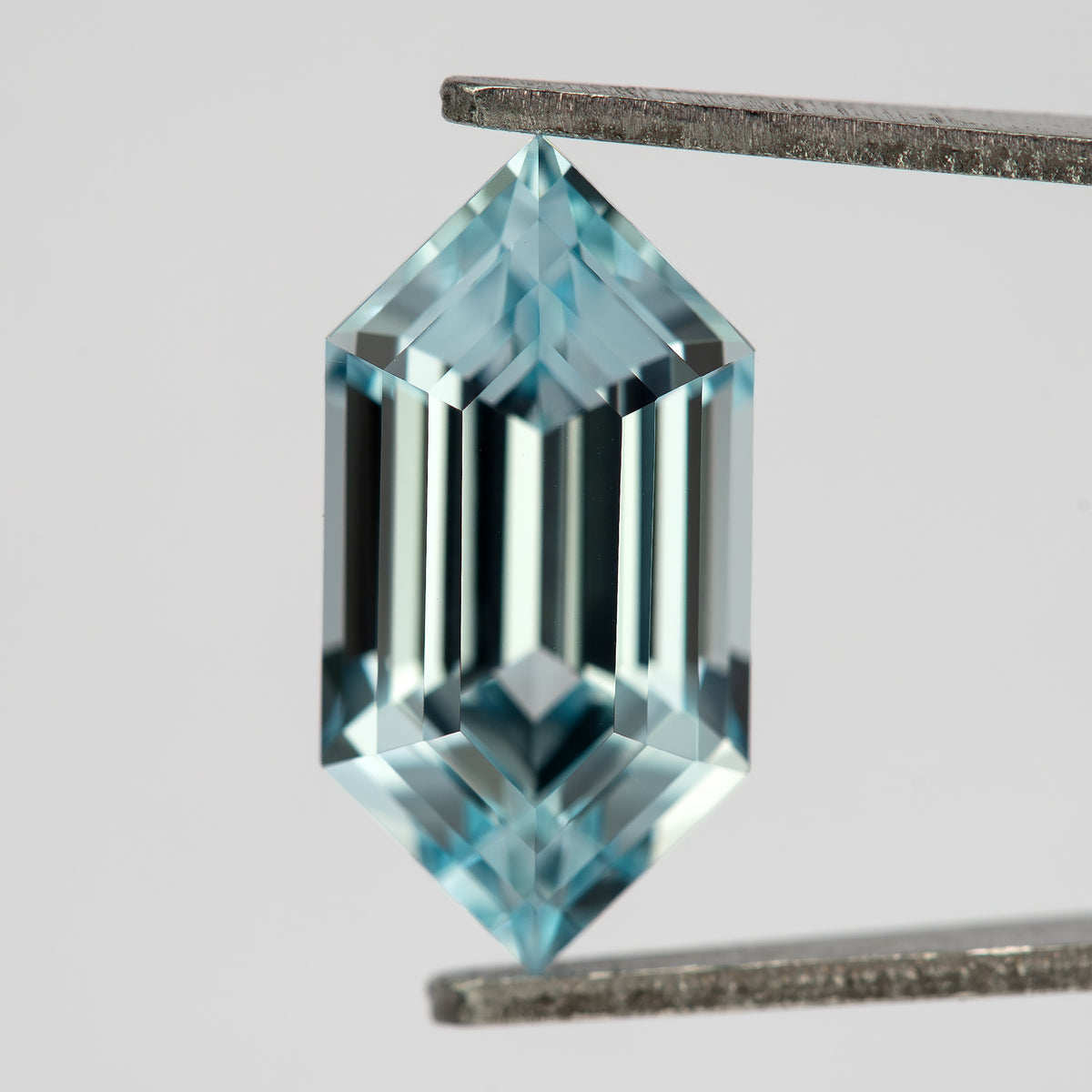 Aqua-blue lab-grown sapphire face-up in tweezers, with alternating dark and bright vertical step reflections.