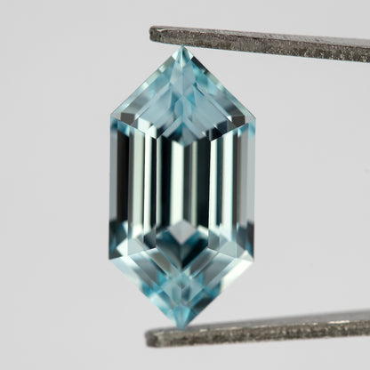 Aqua-blue lab-grown sapphire face-up in tweezers, with alternating dark and bright vertical step reflections.