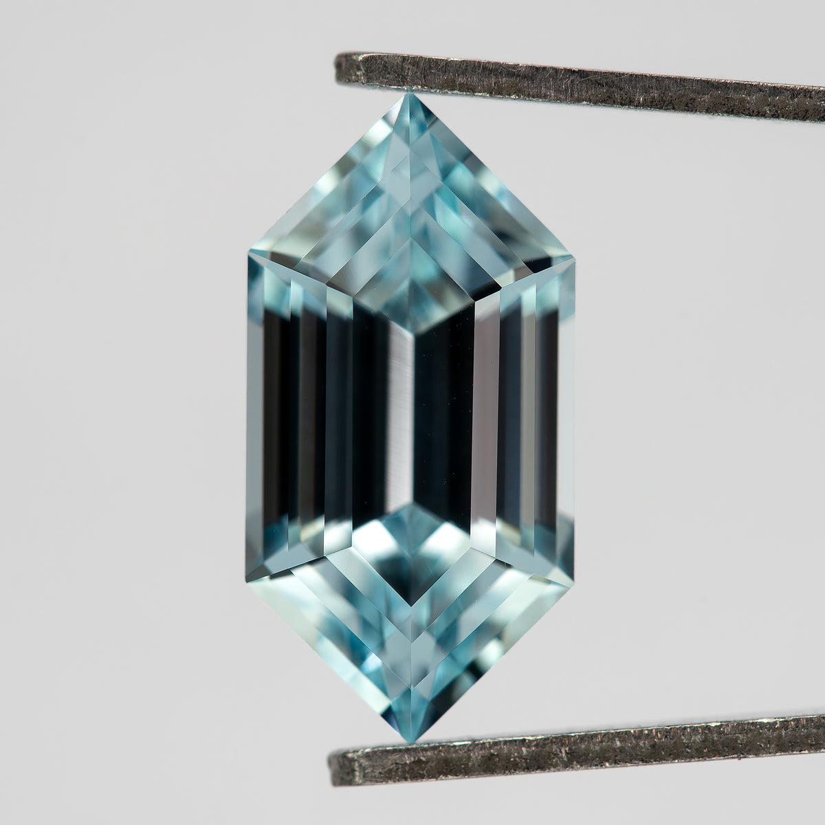 Aqua-blue lab-grown sapphire tilted in tweezers, showing its pointed ends and dark central step reflections.