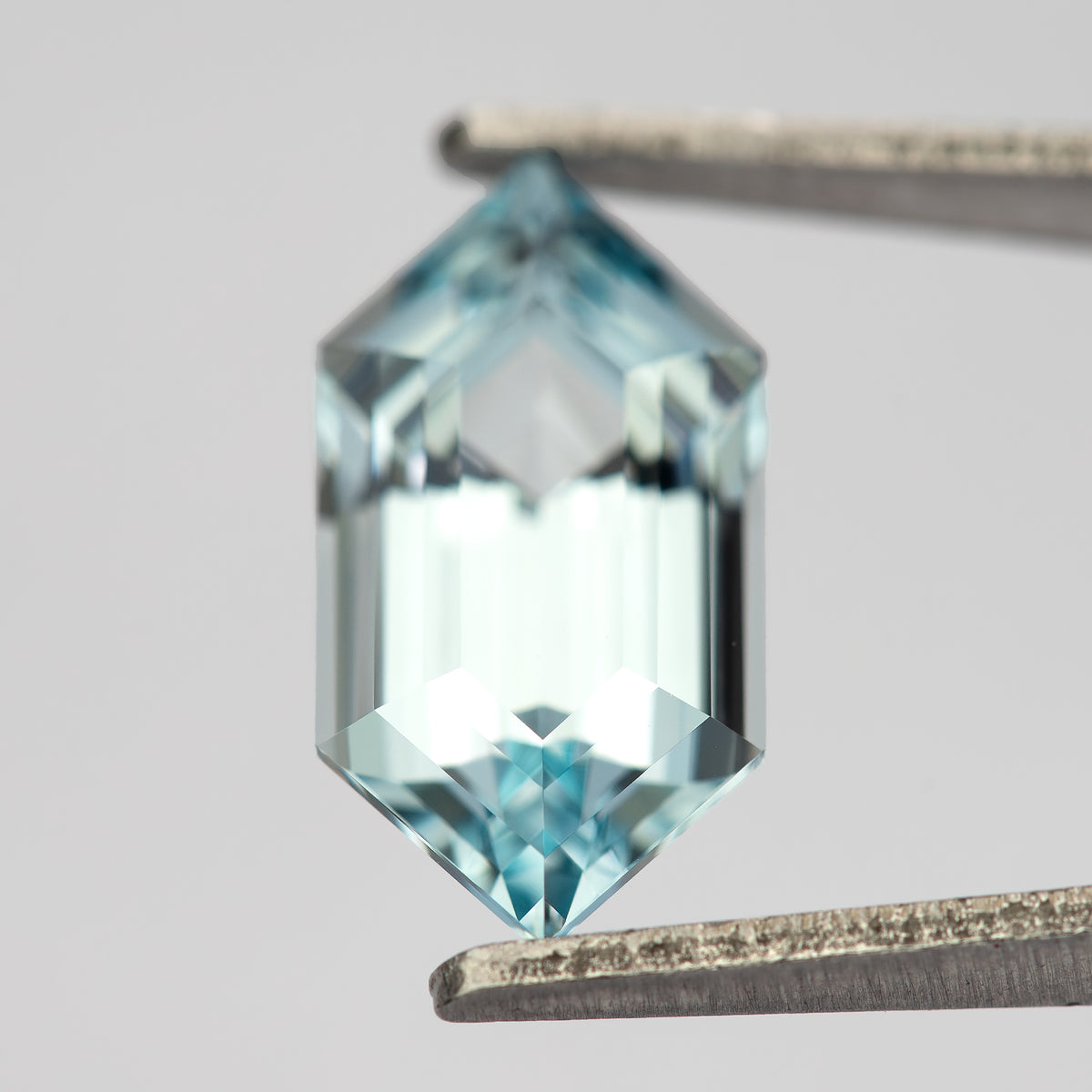 Aqua-blue lab-grown sapphire slightly tilted in tweezers, showing its top point and bright central facets.
