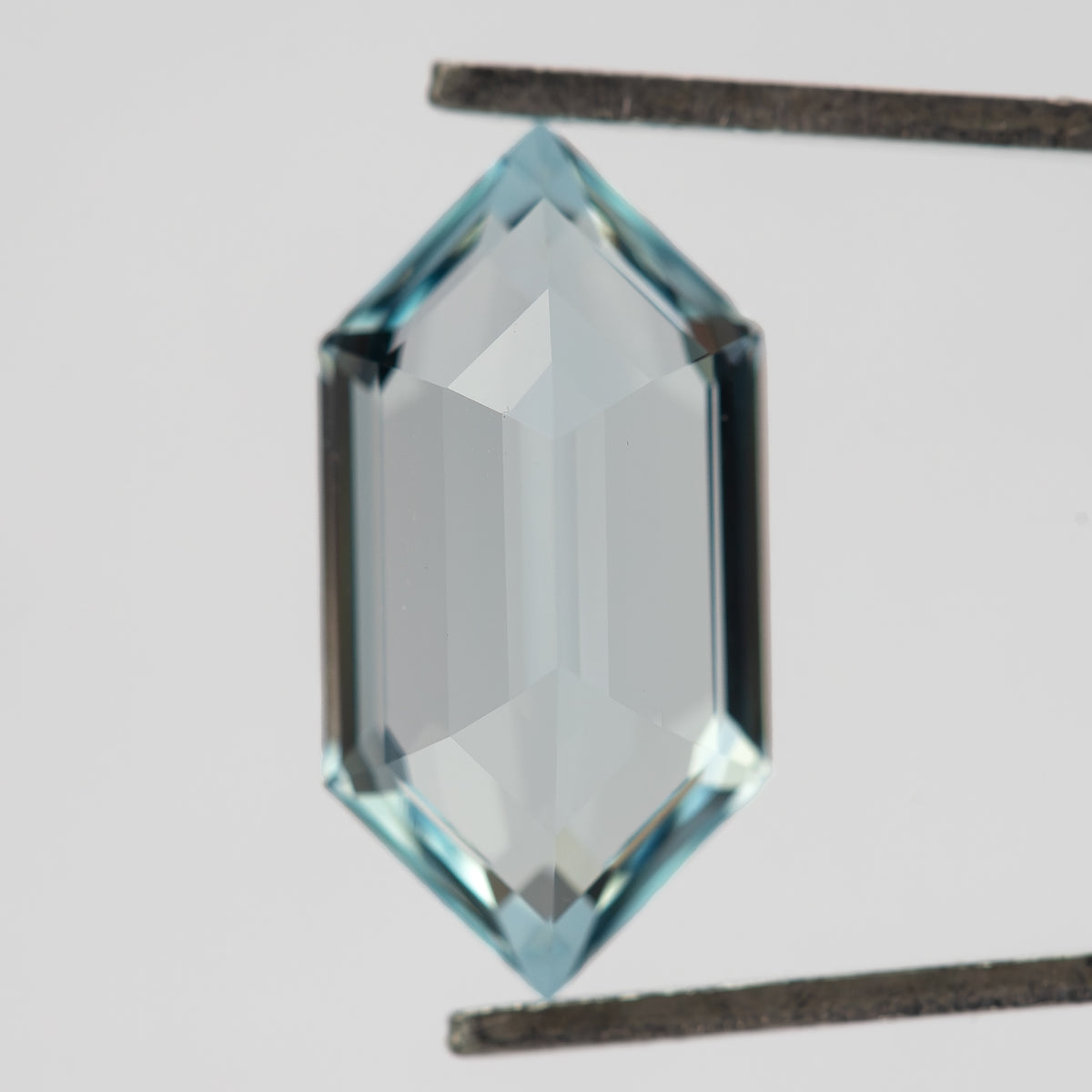 Back-facing view of the aqua-blue lab-grown sapphire in tweezers, showing broad pale pavilion reflections.