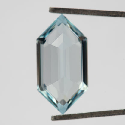 Back-facing view of the aqua-blue lab-grown sapphire in tweezers, showing broad pale pavilion reflections.
