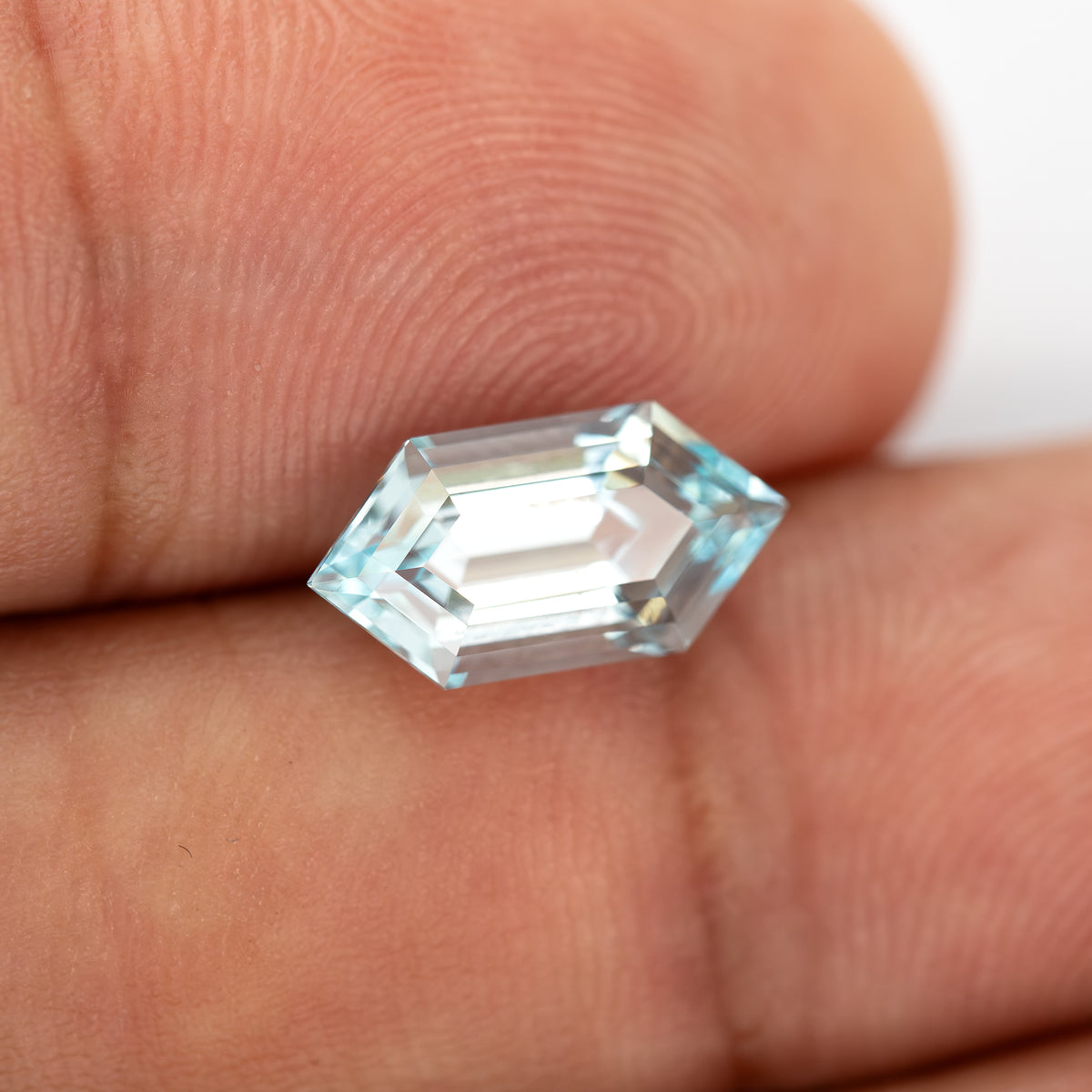 Aqua-blue lab-grown sapphire held at an angle between fingertips, with bright step facets.