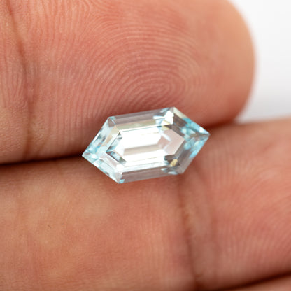 Aqua-blue lab-grown sapphire held at an angle between fingertips, with bright step facets.