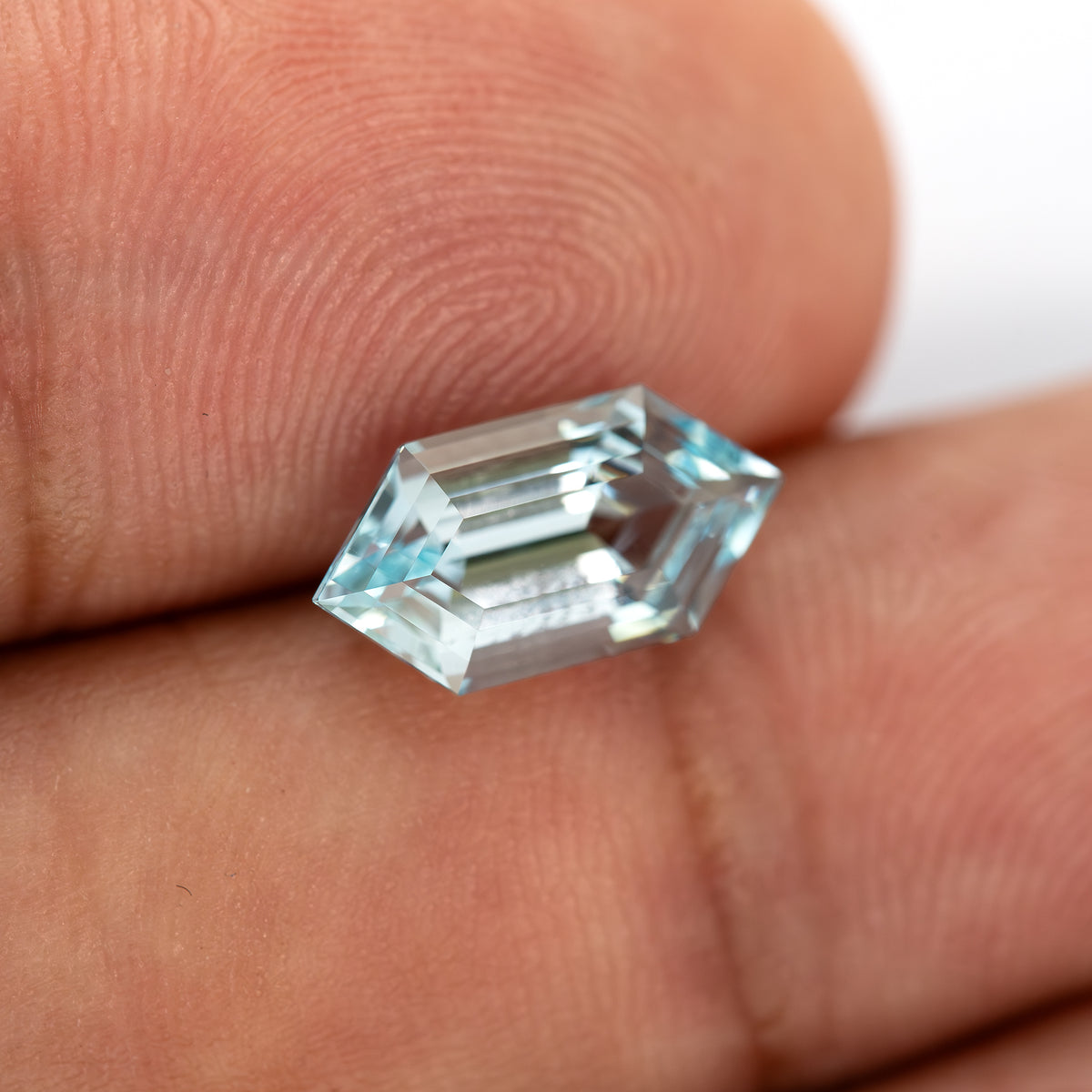 Aqua-blue lab-grown sapphire tilted between fingertips, showing the raised crown and pointed ends.