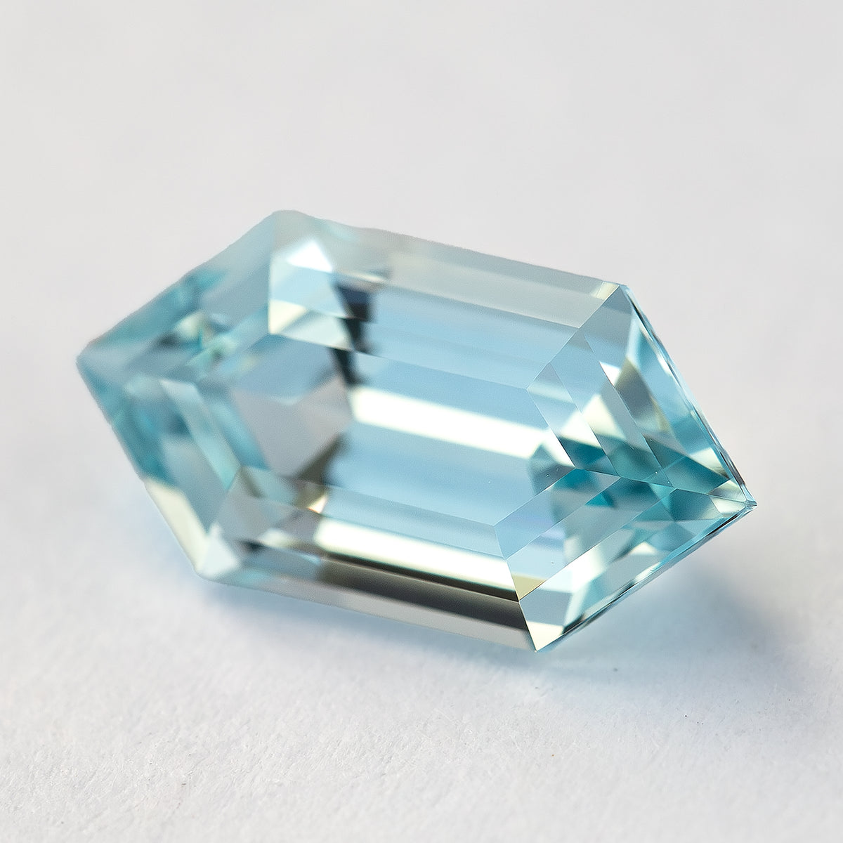 Aqua-blue lab-grown sapphire angled on a pale surface, showing its crown steps and pointed end facets.