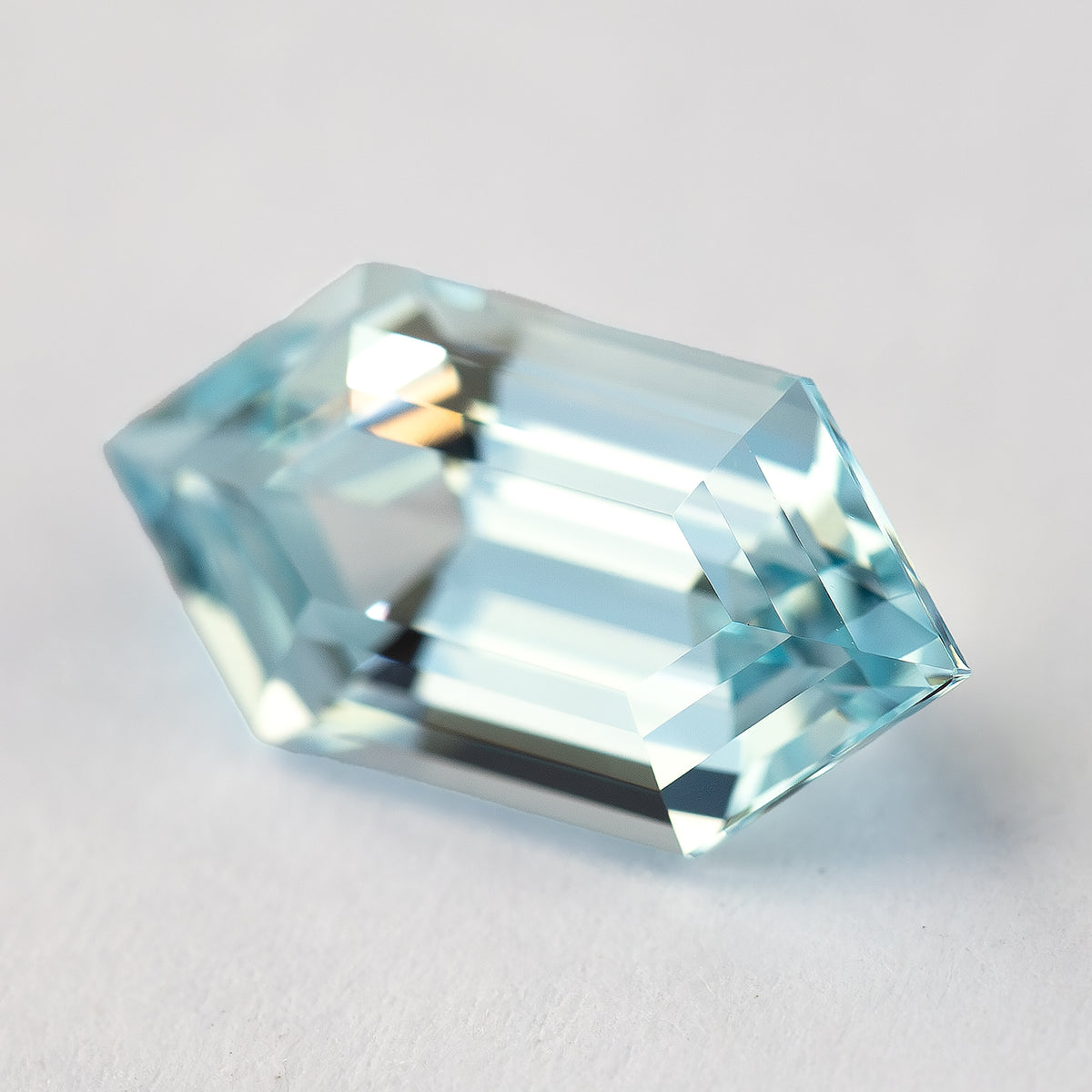 Tilted aqua-blue lab-grown sapphire on a pale surface, with mixed blue and pale reflections across its steps.