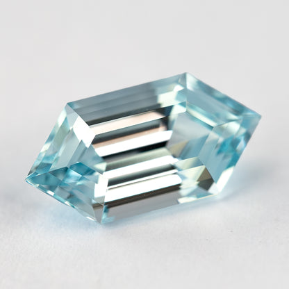 Aqua-blue lab-grown sapphire lying diagonally on a pale surface, with alternating bright and dark step facets.