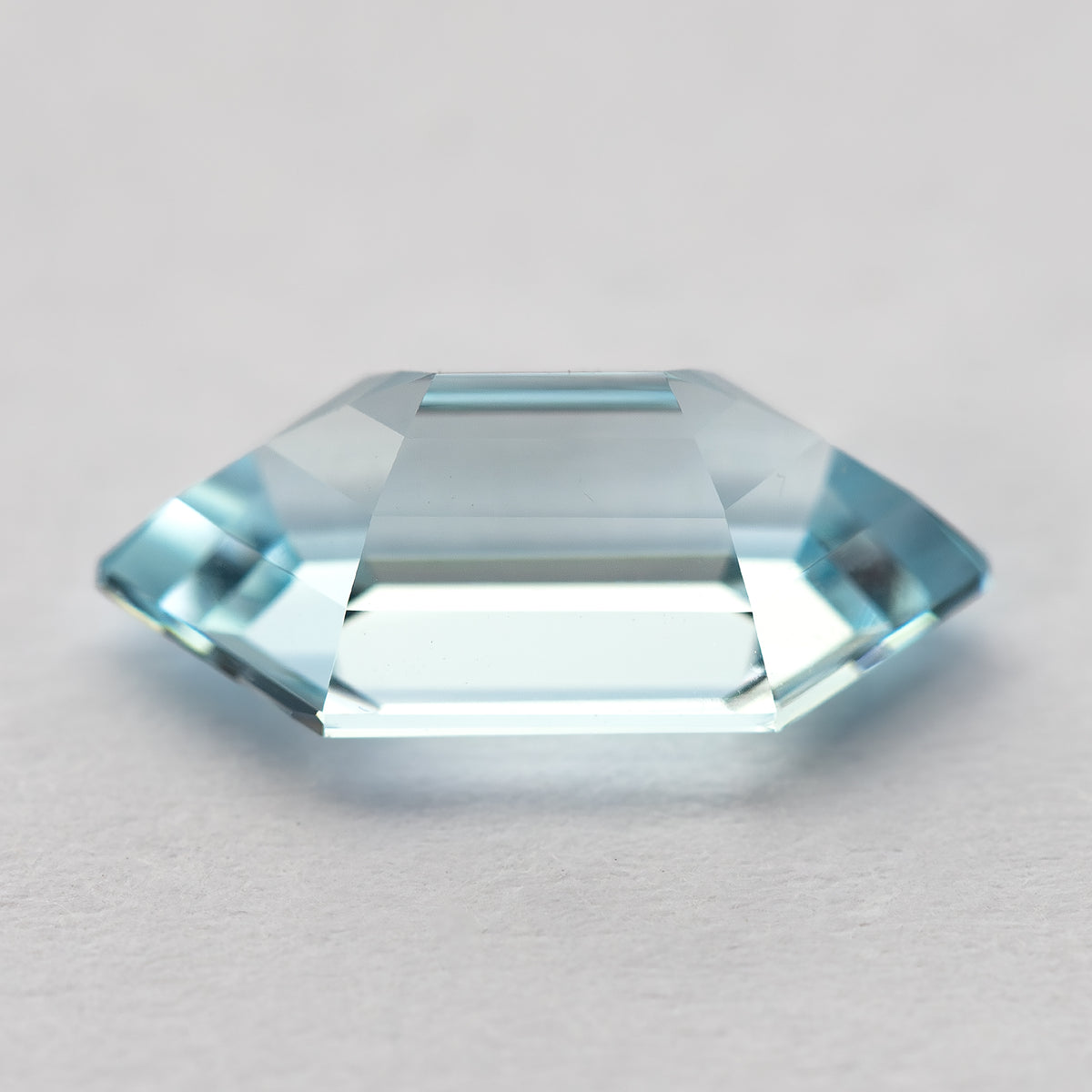 Low side view of the aqua-blue lab-grown sapphire on a pale surface, showing its crown and pavilion.