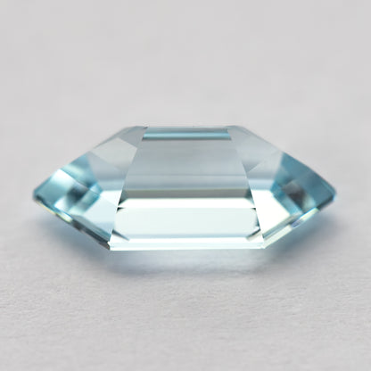 Low side view of the aqua-blue lab-grown sapphire on a pale surface, showing its crown and pavilion.