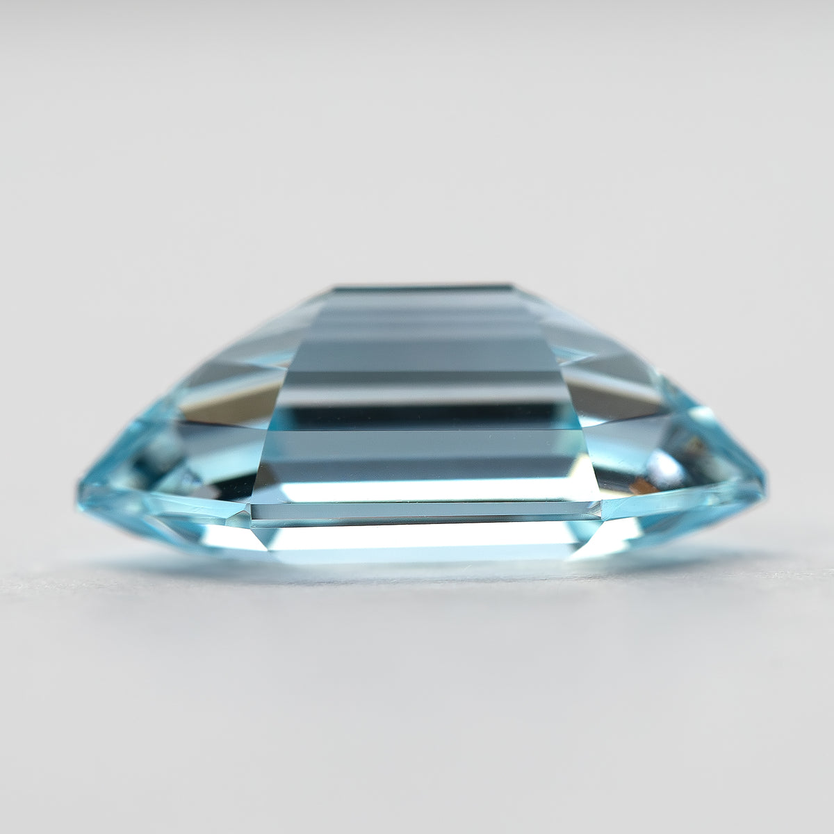 Side profile of the aqua-blue lab-grown sapphire, with long horizontal step facets and pointed ends.