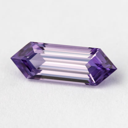 Angled lavender lab-grown sapphire on a pale surface, showing long pale facets and violet pointed ends.