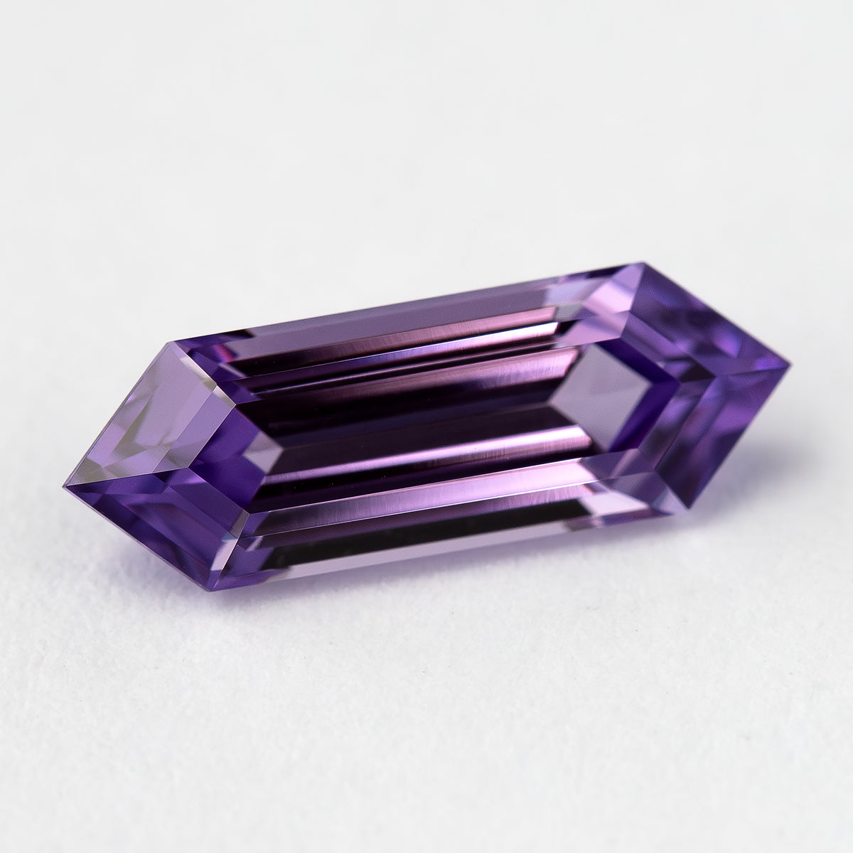Angled lavender lab-grown sapphire on a pale surface, with deep violet and dark central reflections.