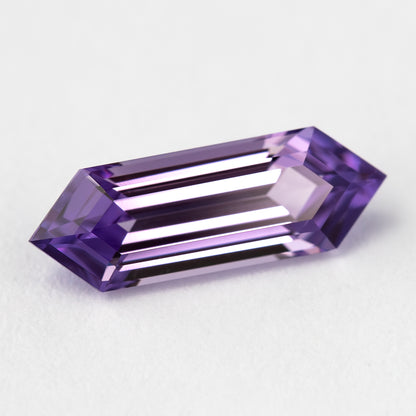 Lavender lab-grown sapphire on a pale surface, showing bright parallel reflections across its long facets.