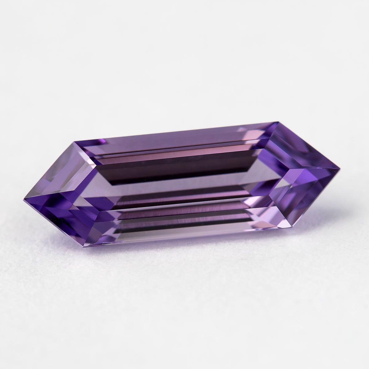 Horizontal lavender lab-grown sapphire on a pale surface, with alternating light and dark violet facets.