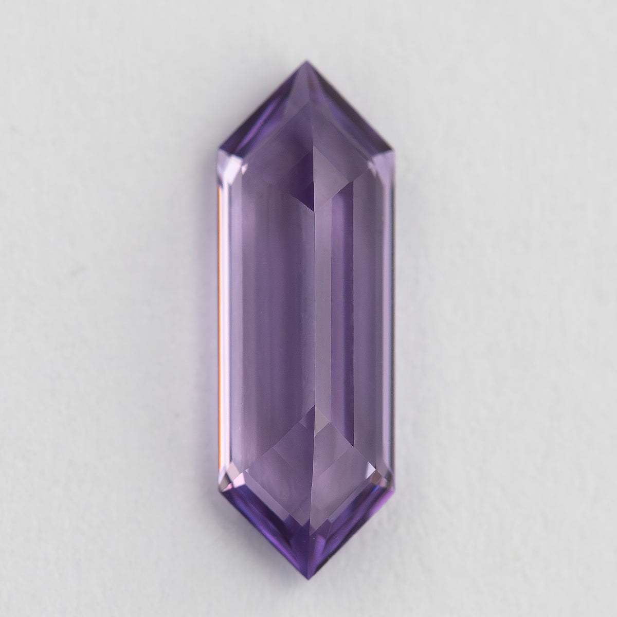 Lavender lab-grown sapphire positioned vertically on a pale surface, showing a broad pale centre and violet edges.