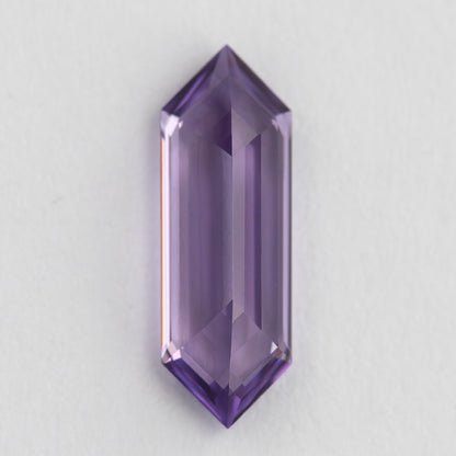Lavender lab-grown sapphire positioned vertically on a pale surface, showing a broad pale centre and violet edges.