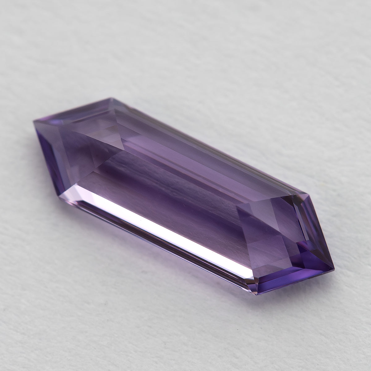 Low angled view of a lavender lab-grown sapphire on a pale surface, showing its profile and violet facets.