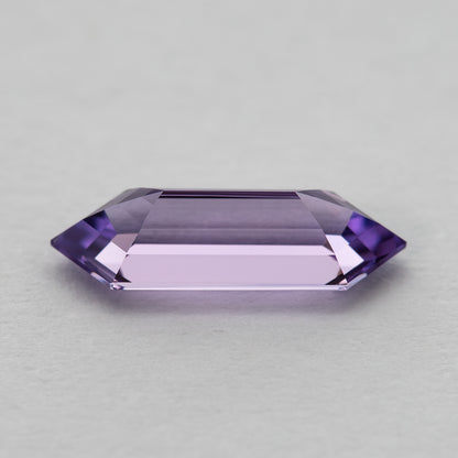 Horizontal view of a lavender lab-grown sapphire on a pale surface, showing a broad pale centre and pointed ends.