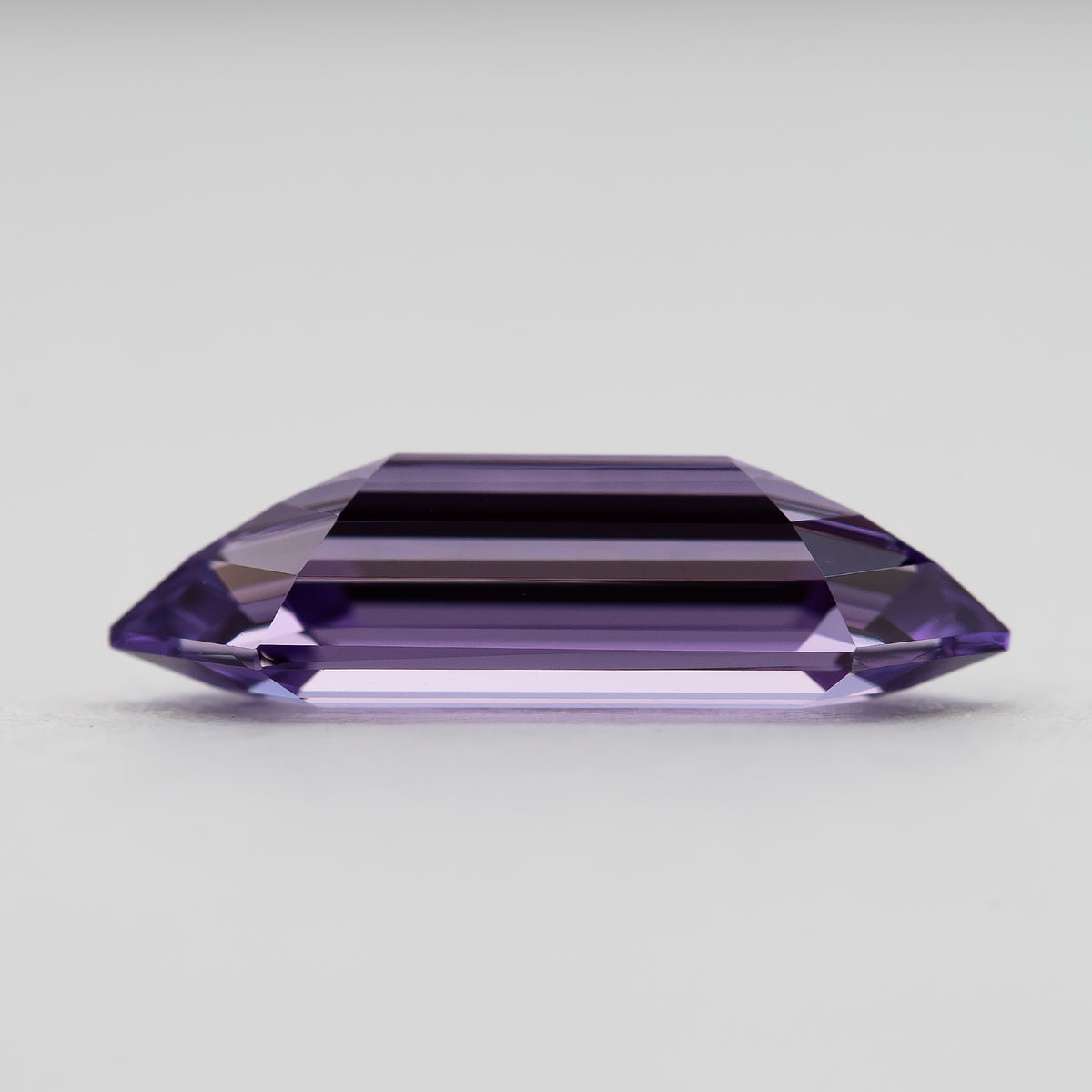 Side profile of a lavender lab-grown sapphire on a pale surface, showing its faceted outline.