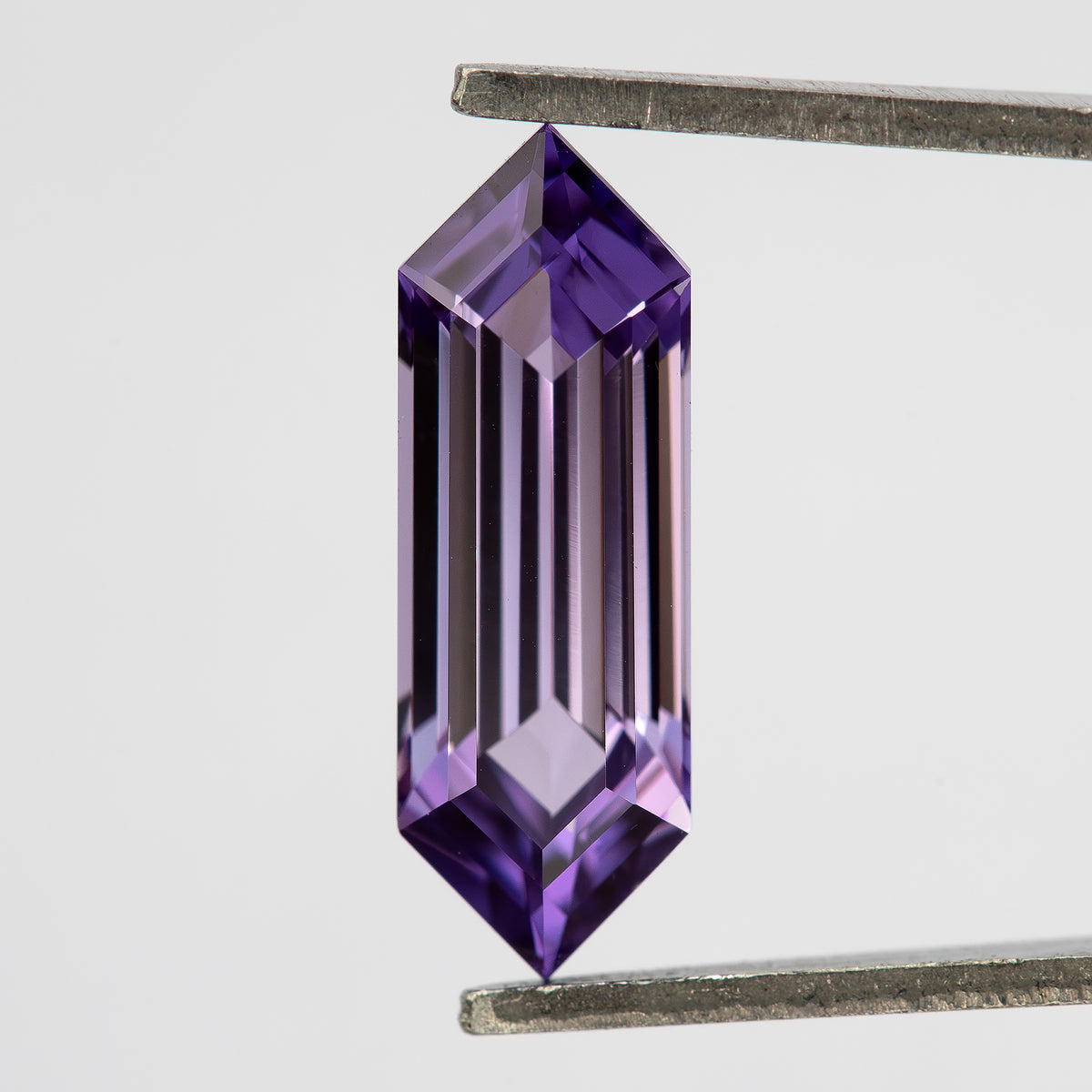 Lavender lab-grown sapphire between tweezers, showing long bright and dark facet reflections.