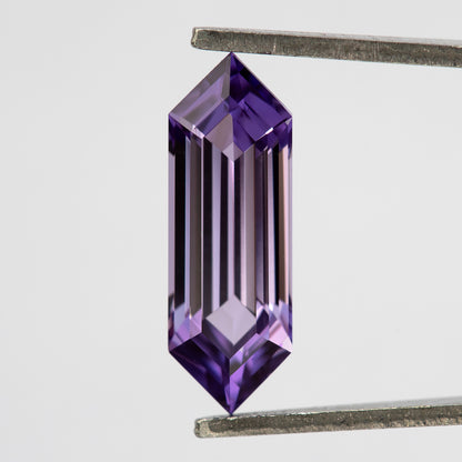 Lavender lab-grown sapphire between tweezers, showing long bright and dark facet reflections.