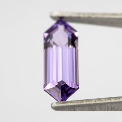 Lavender lab-grown sapphire held vertically between tweezers, with a pale centre and violet pointed ends.