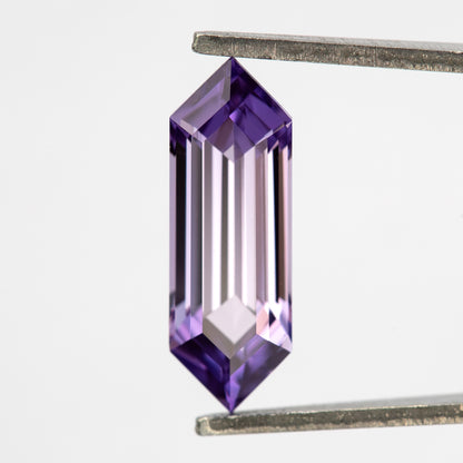 Lavender pink-violet lab-grown sapphire held upright between tweezers, showing its elongated hexagonal shape.