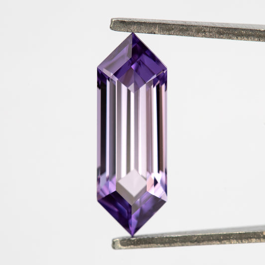 Lavender pink-violet lab-grown sapphire held upright between tweezers, showing its elongated hexagonal shape.