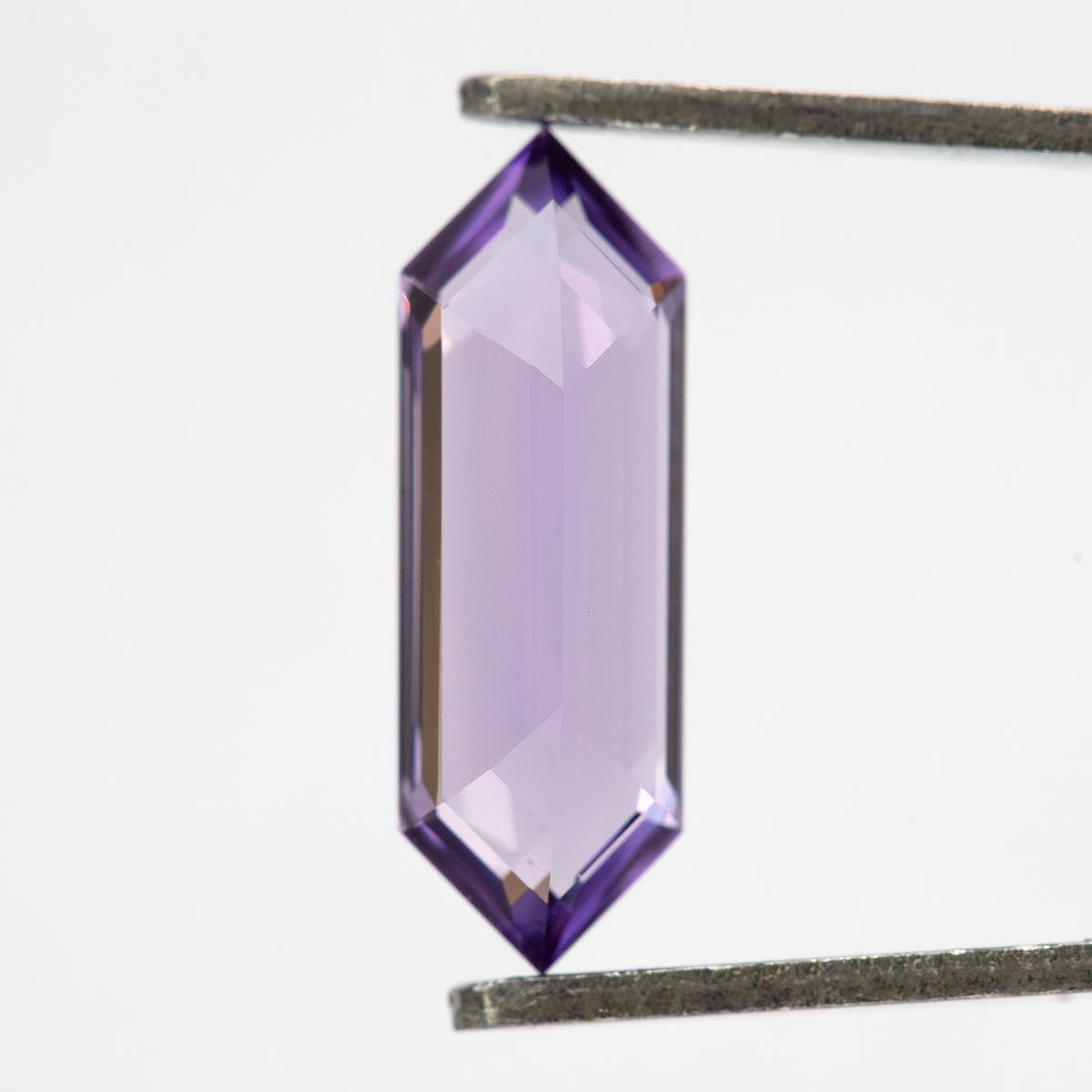 Lavender lab-grown sapphire between tweezers, showing a broad pale central area and violet edges.