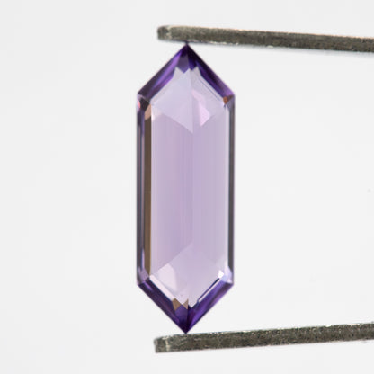 Lavender lab-grown sapphire between tweezers, showing a broad pale central area and violet edges.