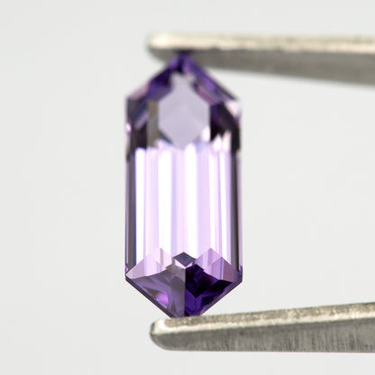 Lavender lab-grown sapphire between tweezers, showing bright central reflections and violet edge facets.