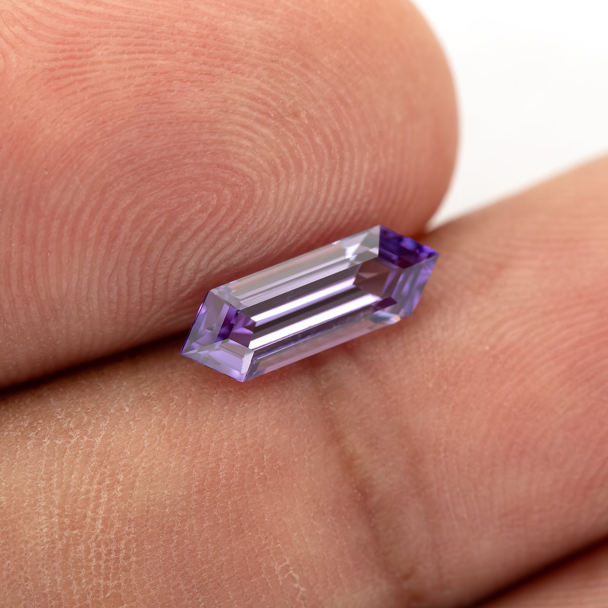 Lavender lab-grown sapphire resting diagonally against fingers, showing its long hexagonal outline.