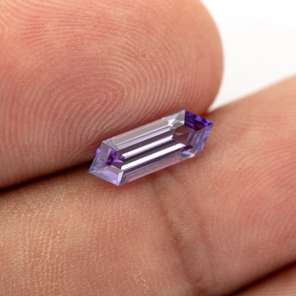 Lavender lab-grown sapphire resting diagonally against fingers, showing its long hexagonal outline.
