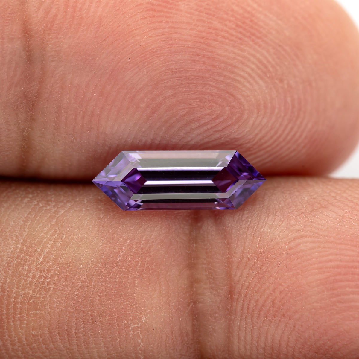 Lavender lab-grown sapphire resting horizontally against fingers, with bright central facet reflections.