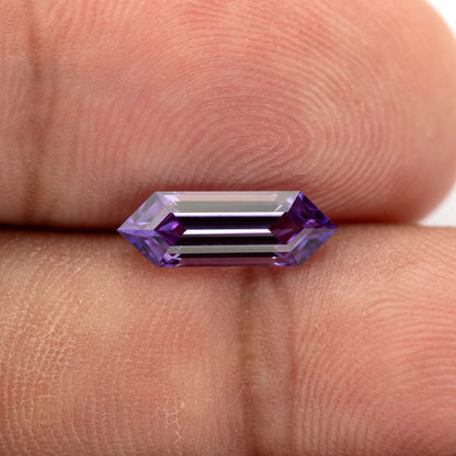 Lavender lab-grown sapphire resting horizontally against fingers, with bright central facet reflections.