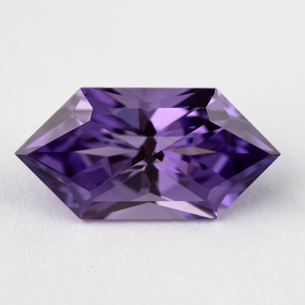 Face-up violet purple lab-grown sapphire with an elongated hexagon outline and angular facets on a light background.