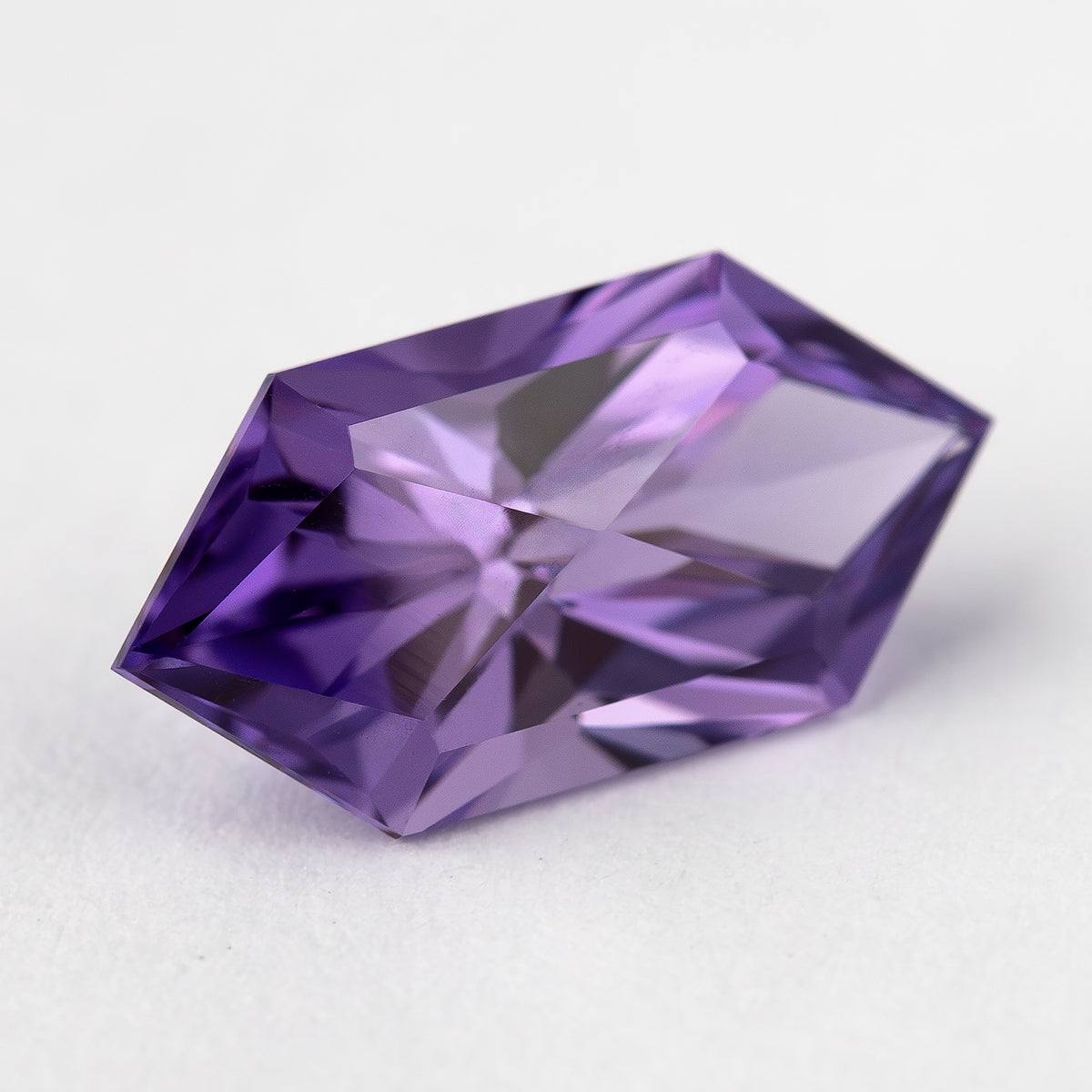 Oblique view of the violet purple lab-grown sapphire, showing its elongated shape and facet reflections.