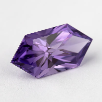 Oblique view of the violet purple lab-grown sapphire, showing its elongated shape and facet reflections.