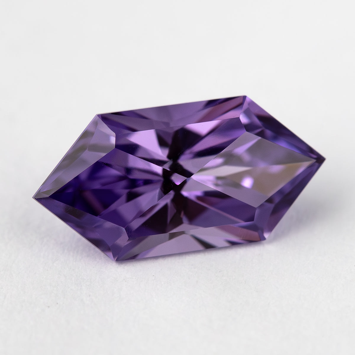 Angled face-up view of the violet purple elongated hexagon sapphire on a light background.