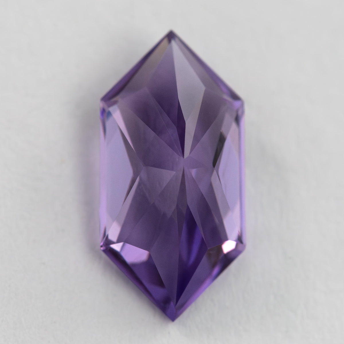 Reverse view of the violet elongated hexagon sapphire, showing its pavilion facets and central ridge.