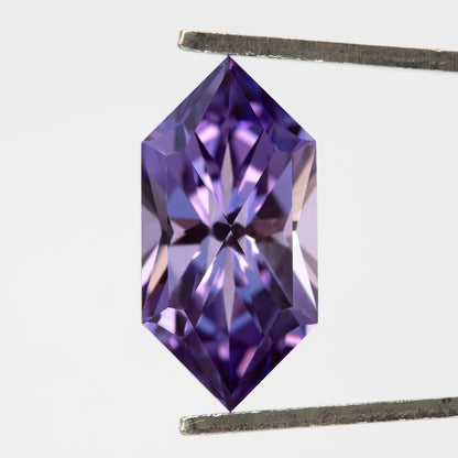 Violet purple elongated hexagon lab-grown sapphire held upright in tweezers, showing face-up faceting.