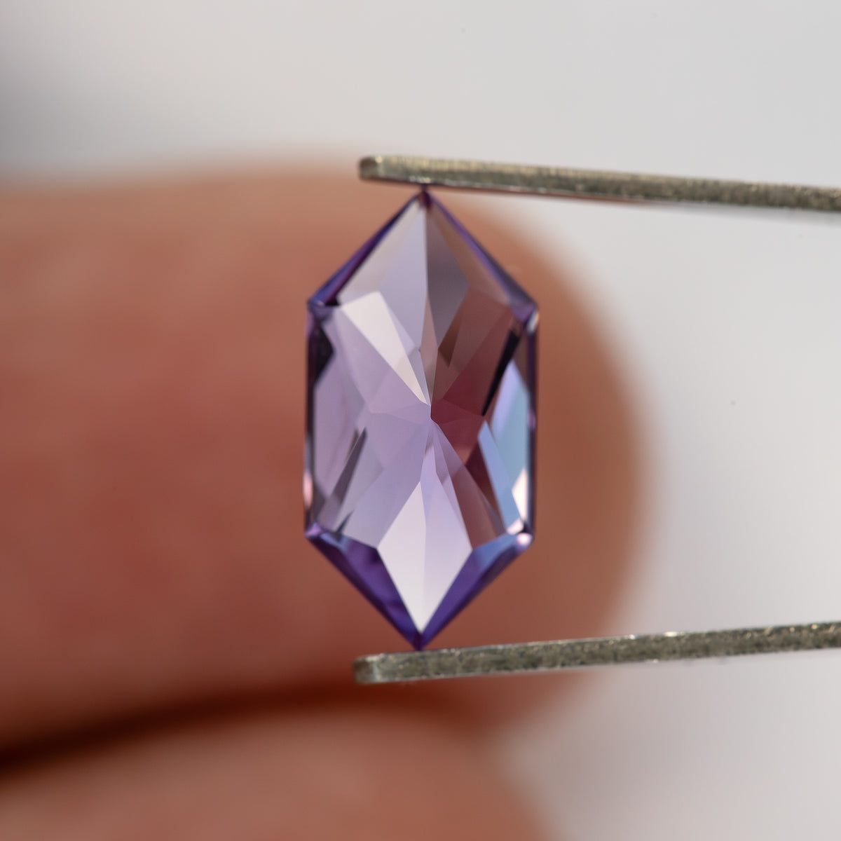 Reverse view of the violet sapphire held near fingers, showing broad pavilion facets.