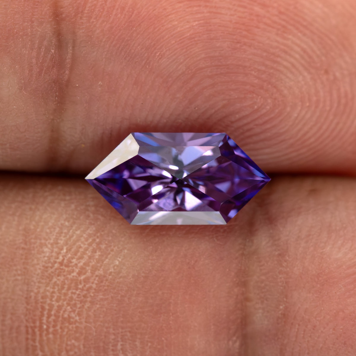 Violet purple elongated hexagon lab-grown sapphire resting on a fingertip.