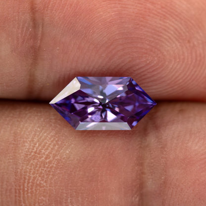 Violet purple elongated hexagon lab-grown sapphire resting on a fingertip.