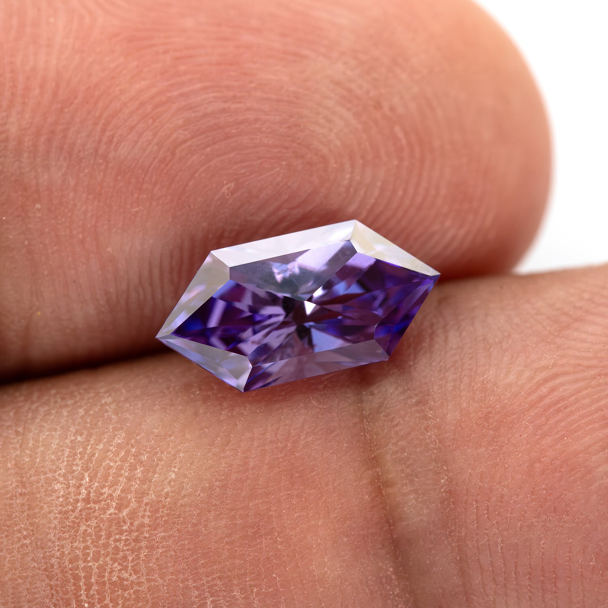 Violet lab-grown sapphire shown against fingers with its geometric outline visible.