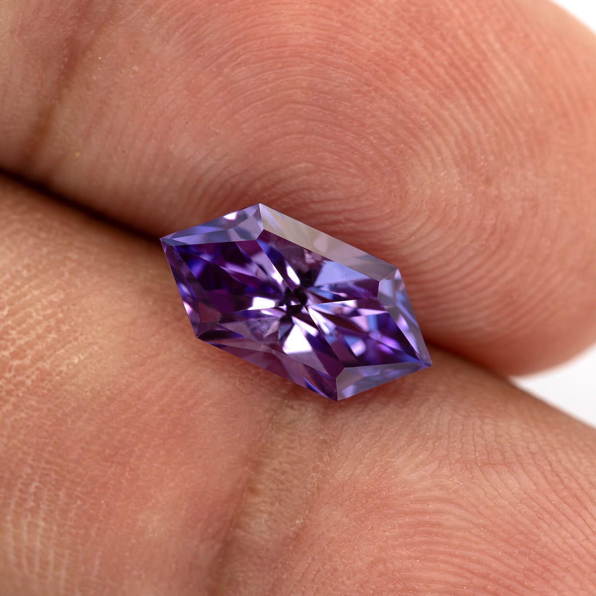 Close view of the violet purple lab-grown sapphire on skin, showing its elongated hexagon proportions.