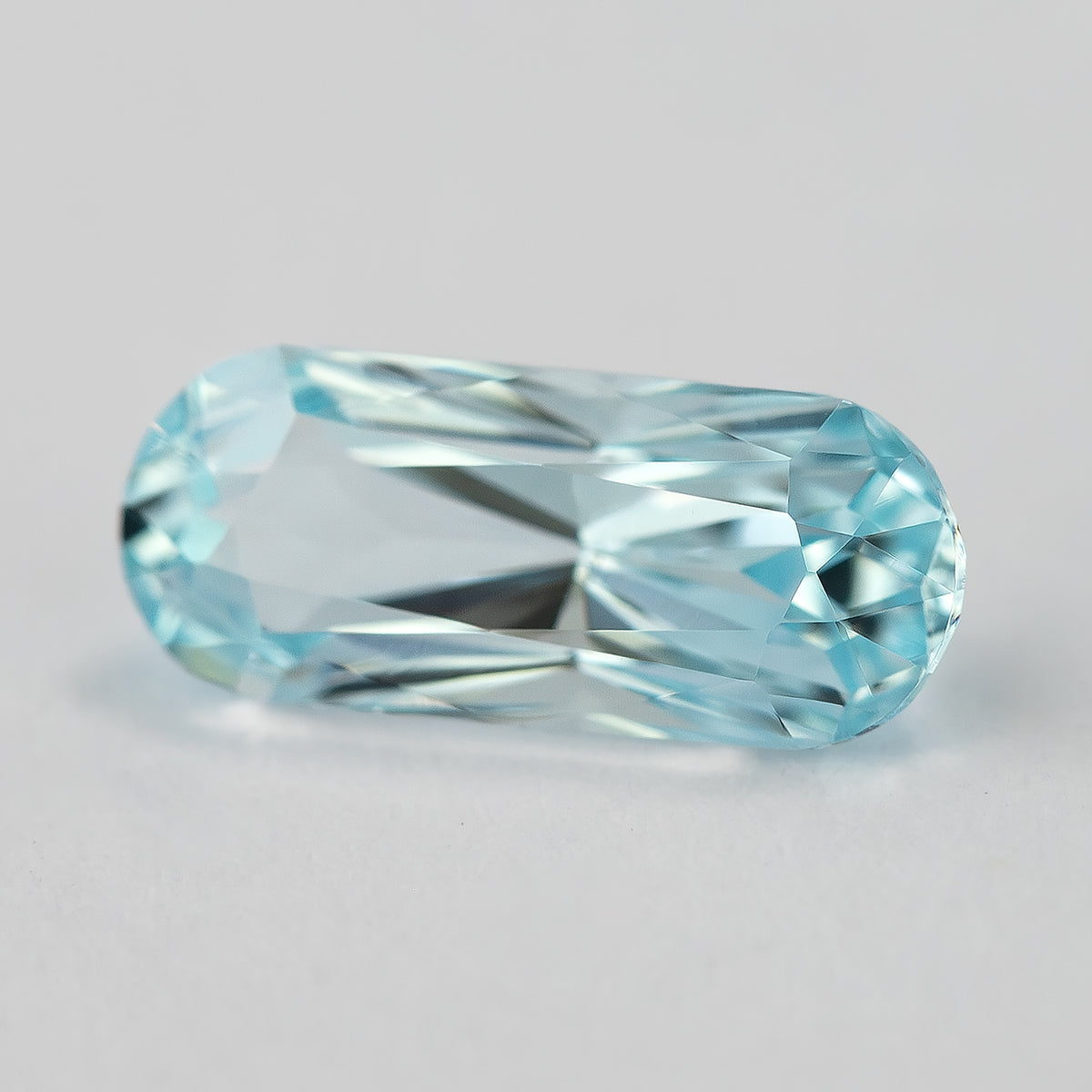 Light blue sapphire at a slight angle, showing broad facet reflections and rounded ends.