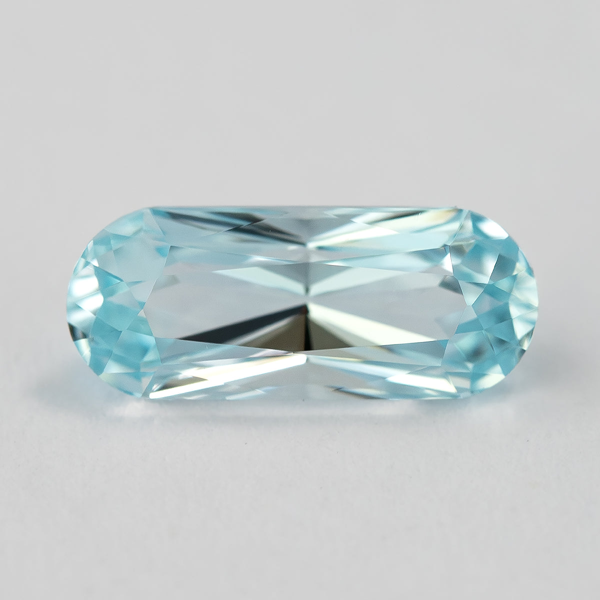 A second face-up view of the elongated light blue sapphire on a pale surface.