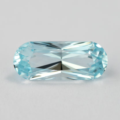 A second face-up view of the elongated light blue sapphire on a pale surface.